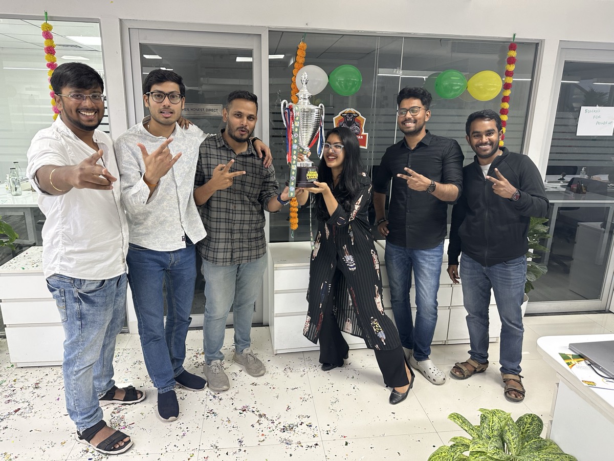 Shahala and teammates holding a trophy in a confetti-covered office decorated with marigolds