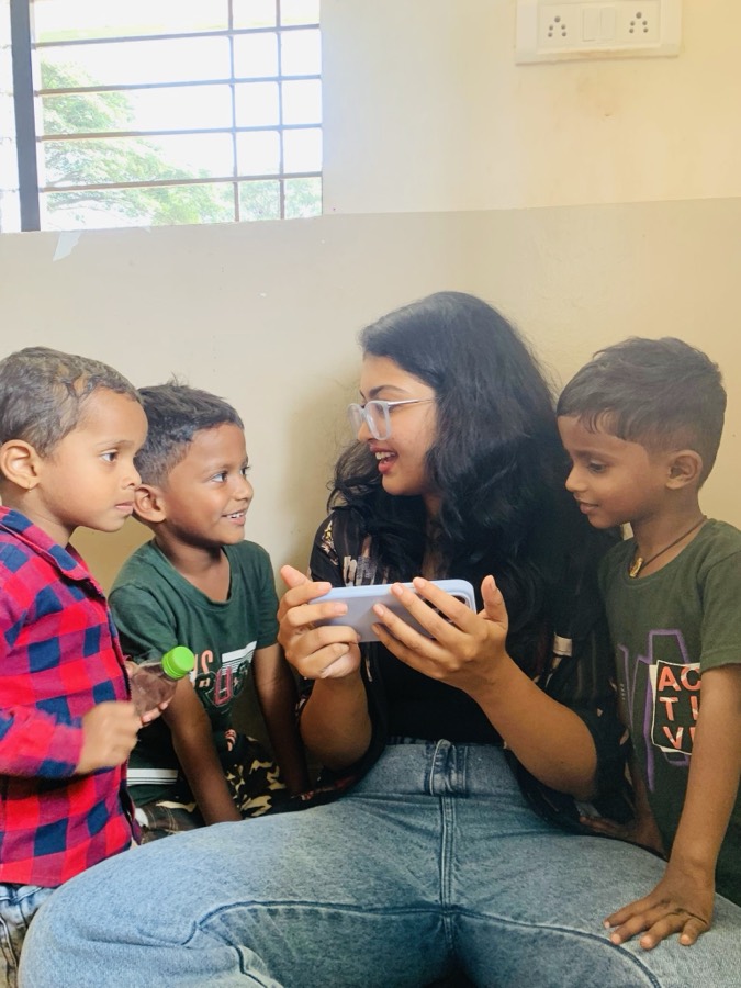 Shahala sitting with three children from the village, showing them something on a phone